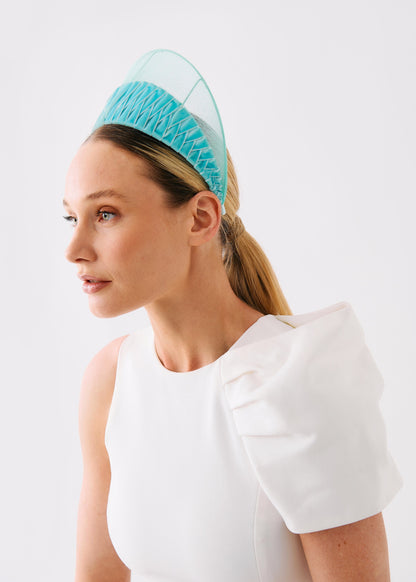 A woman in a white dress wearing a light blue pleated headband with a sheer mesh top, photographed against a plain white background.