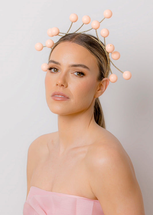 Woman wearing a pink strapless dress and beaded headpiece against a plain background