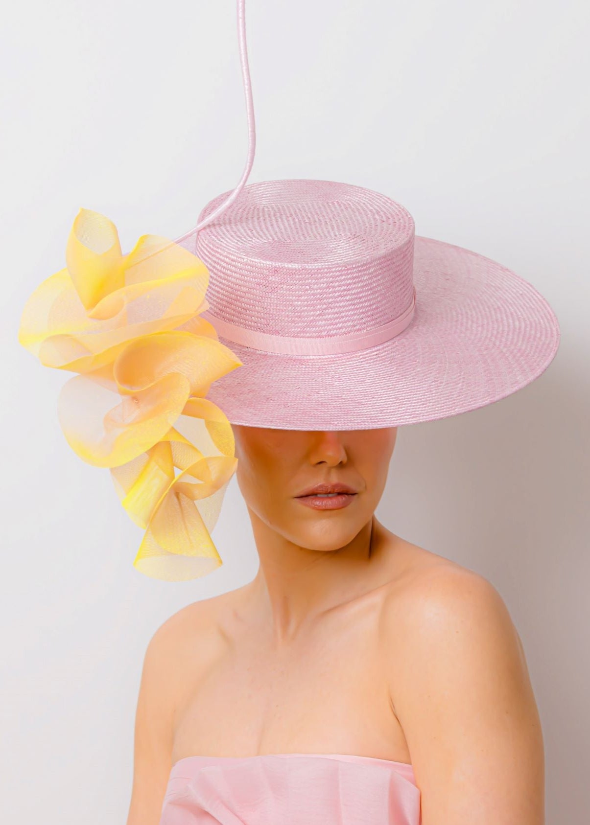 Woman wearing a pink dress and hat with yellow floral trim against a white background