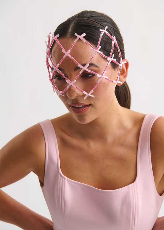 Woman wearing a pink face veil with a grid design on a plain background