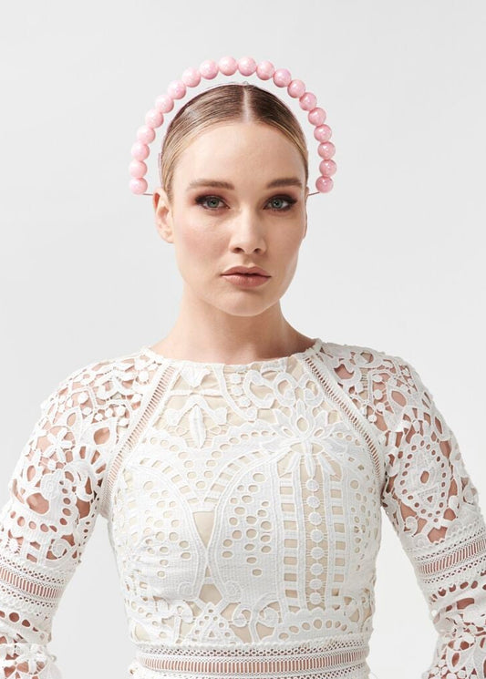 Woman wearing a white lace dress with a pink beaded headband on a light gray background