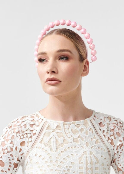 Woman wearing a white lace dress with a pink beaded headband on a light gray background