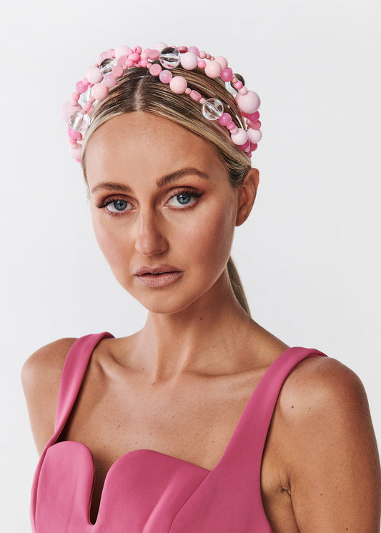 Woman wearing a pink dress and beaded headband against a white background