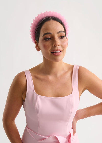 Woman wearing a pink dress and headband against a white background