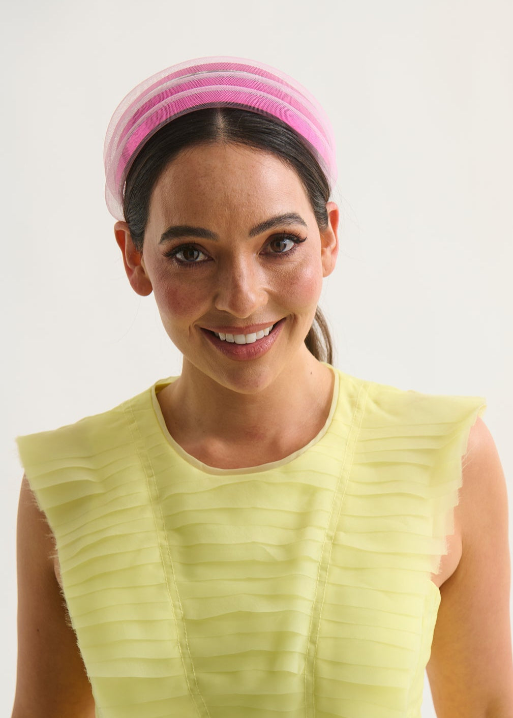 Woman wearing a yellow sleeveless top and pink headband against a white background