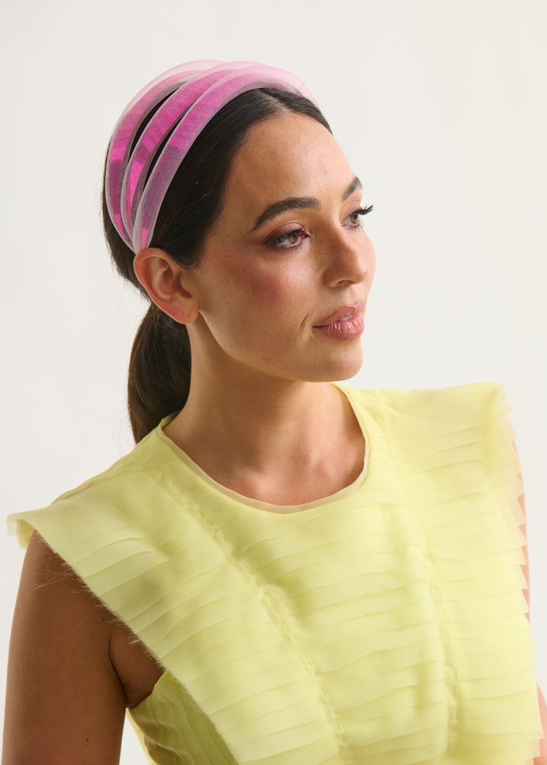 Woman wearing a yellow top and pink headband against a white background