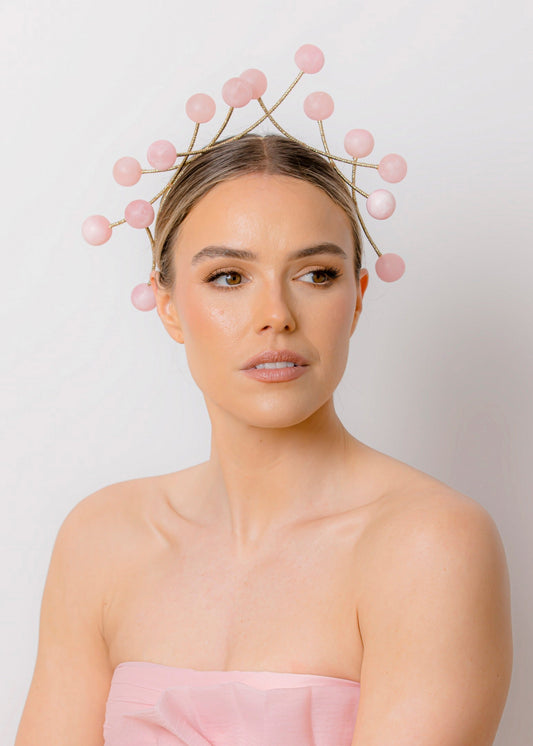 Woman wearing a pink strapless dress and bead headpiece against a plain background