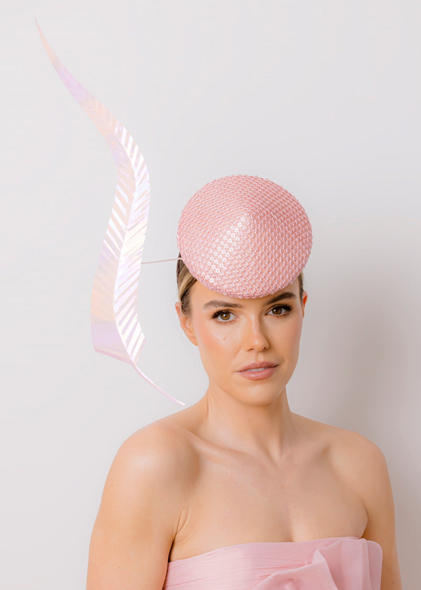 Woman wearing a pink dress and hat with a feather against a white background