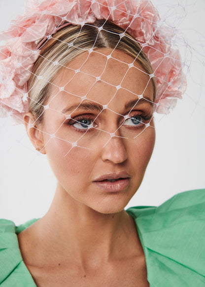 Woman wearing a pink face veil with a white background