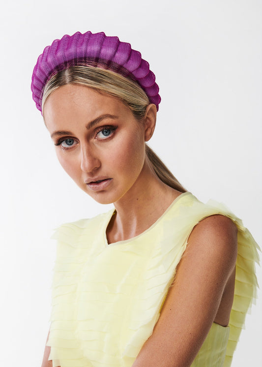 Woman wearing a yellow dress and purple headband against a white background
