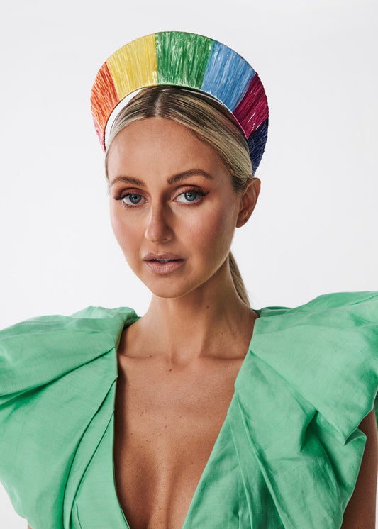 Woman wearing a colorful rainbow raffia headband and green dress on a white background