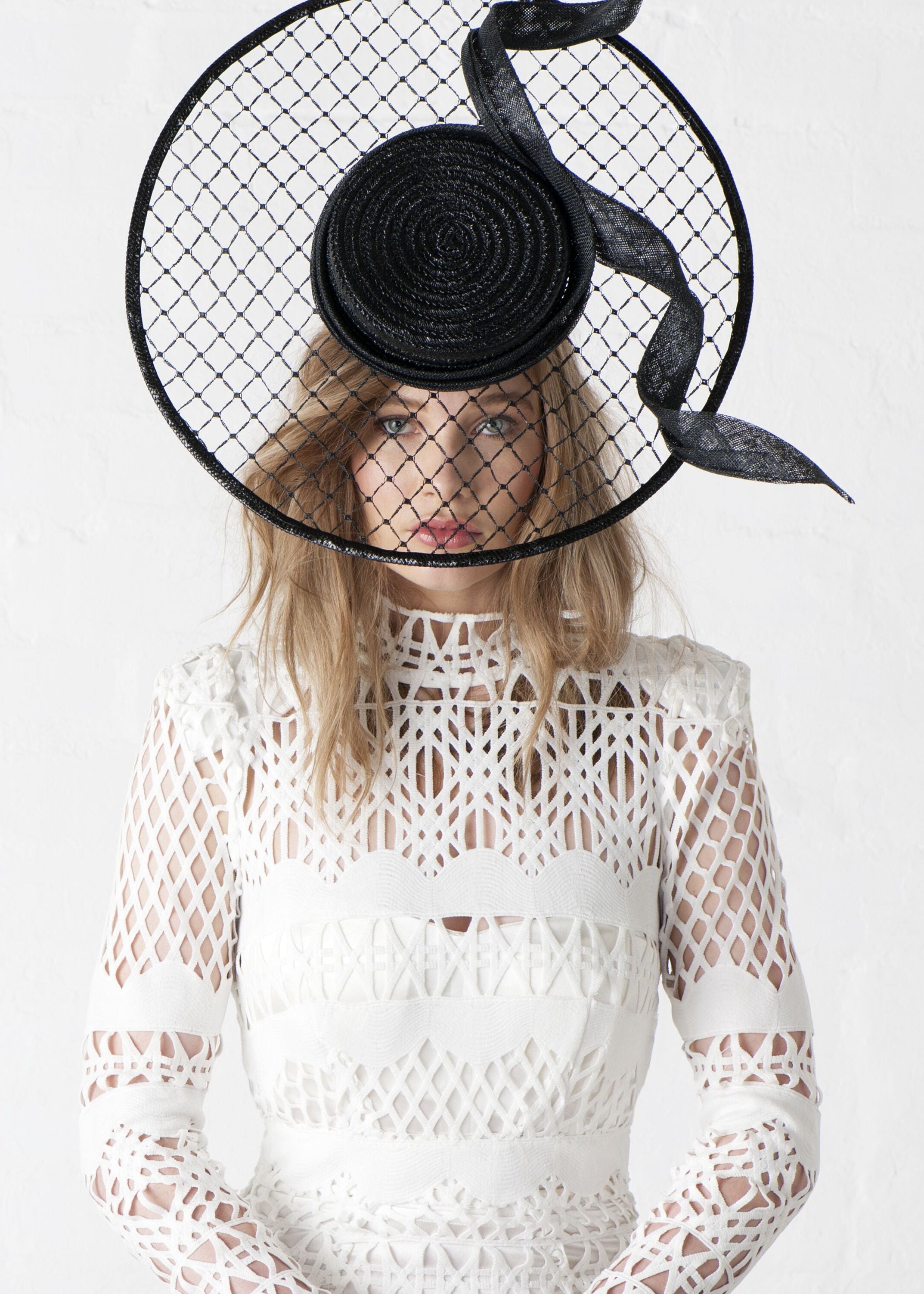 Woman wearing a white lace dress and a black hat with a wide brim on a white background