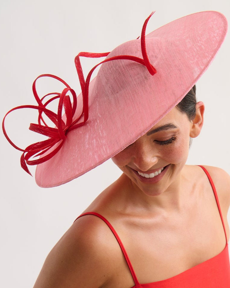 Woman wearing a red dress and pink hat with a decorative bow on a white background