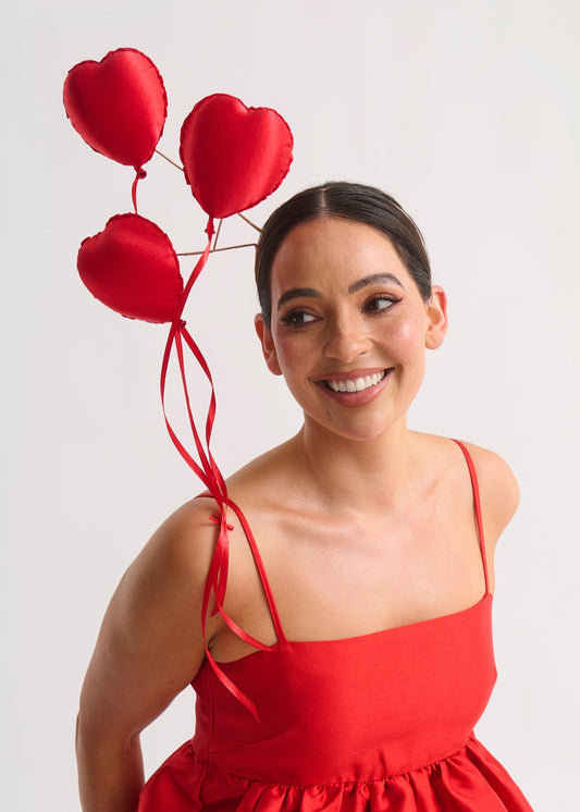 Woman in a red dress with a heart-shaped balloon headpiece against a white background