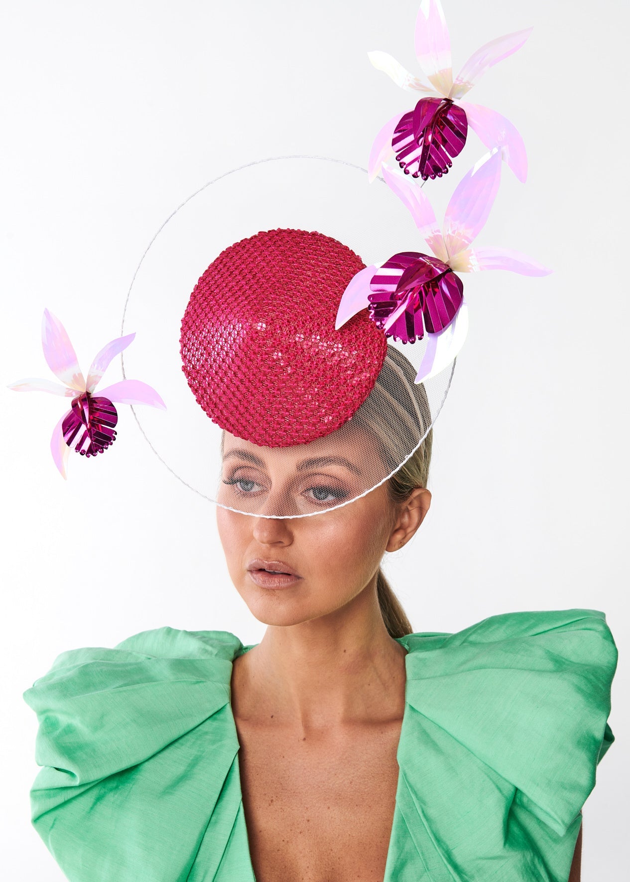 Woman wearing a bright pink headpiece with floral elements on a white background