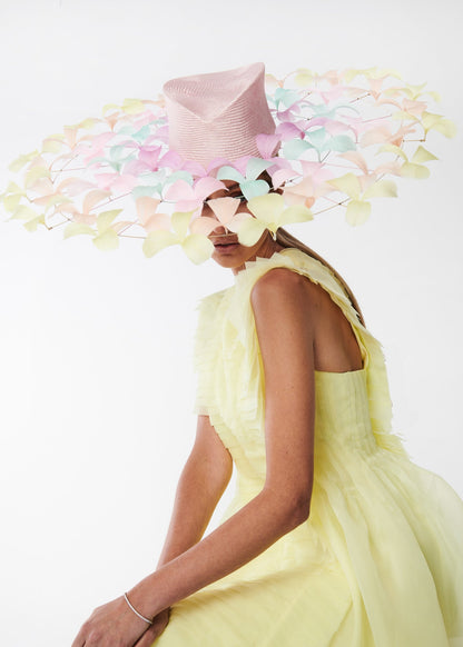 Woman wearing a bright yellow dress and a colorful hat with pastel flowers on a white background