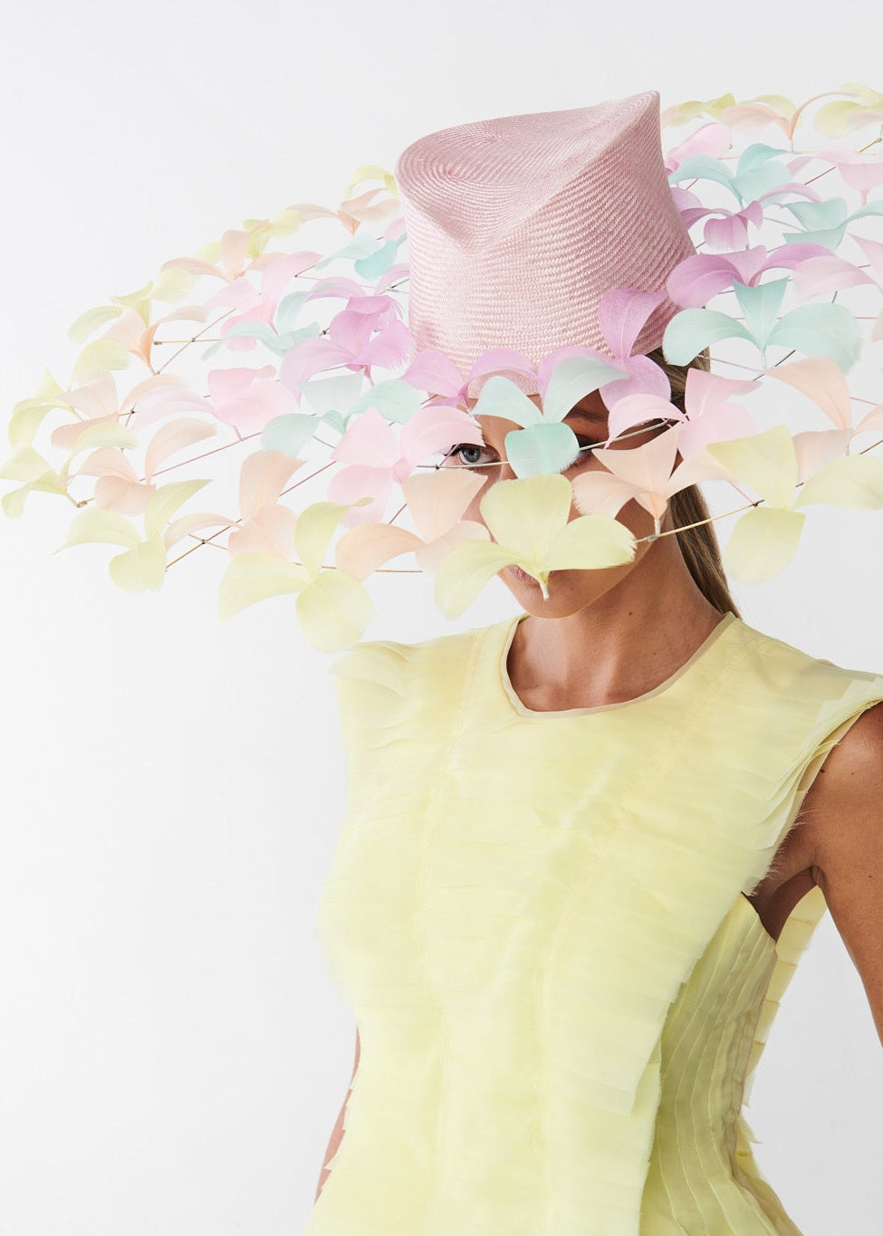 Woman wearing a yellow dress and a large decorative hat with colorful feathers on a white background
