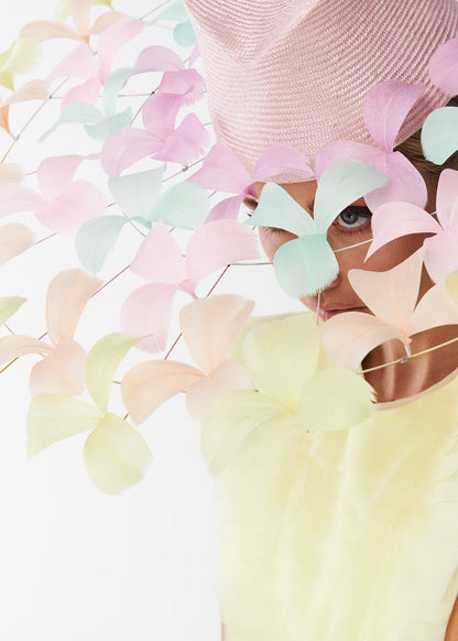 Woman wearing a pastel-colored feather brimmed hat and dress on a light background