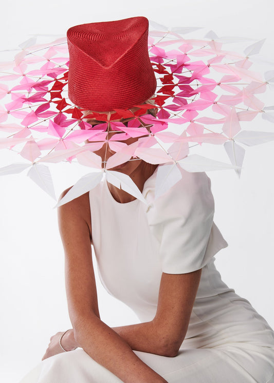 Person wearing a white dress and red and pink feather brimmed hat design on a white background