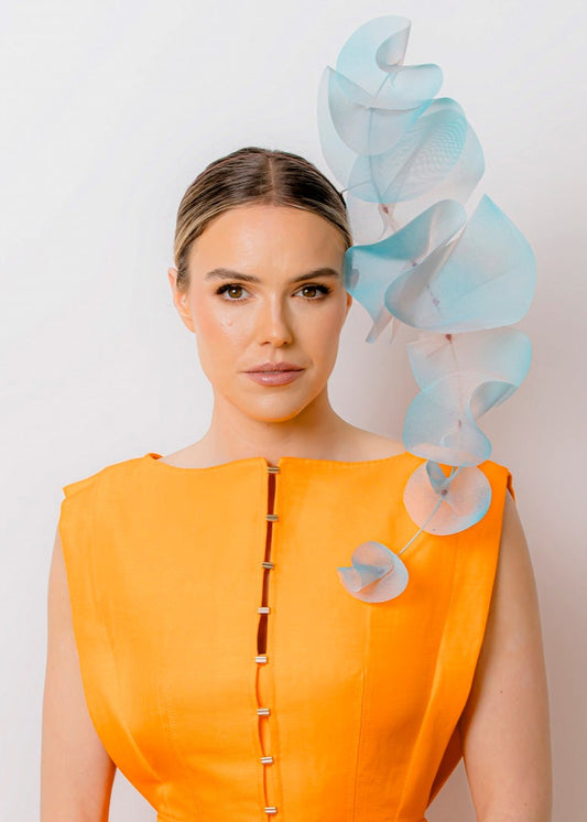 Woman wearing an orange dress with a decorative headpiece against a plain background