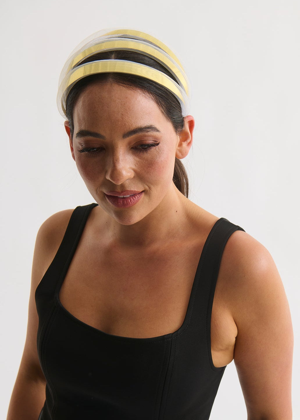 Woman wearing a black sleeveless top and gold headband on a white background