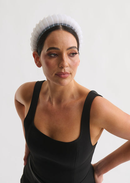 Woman wearing a black sleeveless dress and white headband with a plain white background