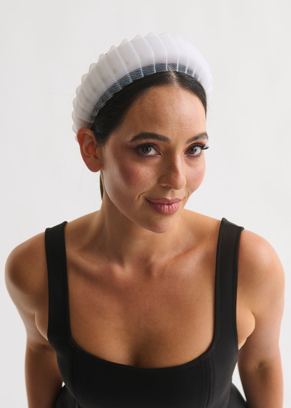 Woman wearing a black dress and white headband against a plain background