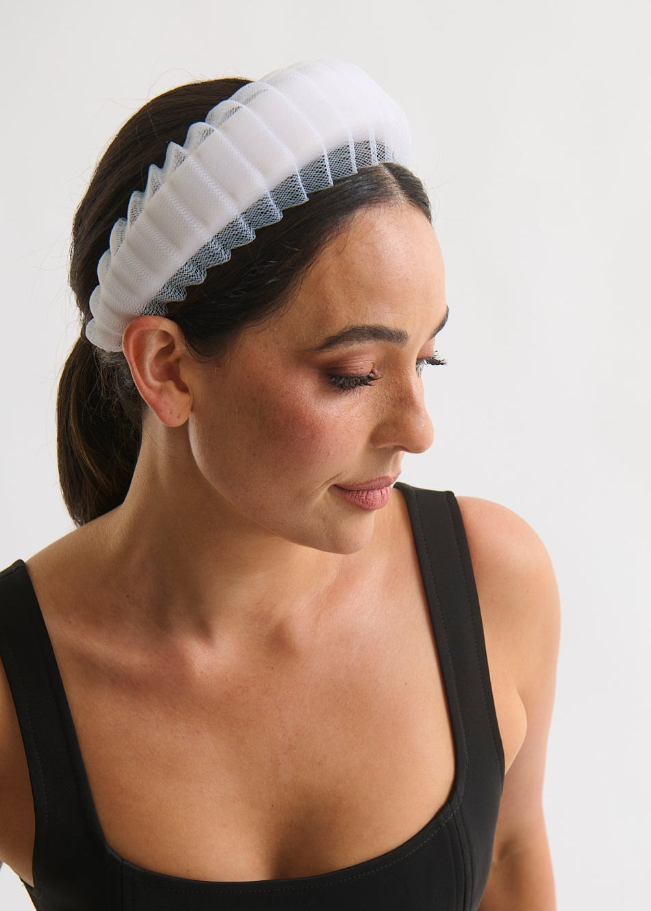 Woman wearing a white headband with a black dress on a plain background