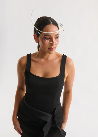 Woman wearing a white feather quill headpiece and a black dress against a white background