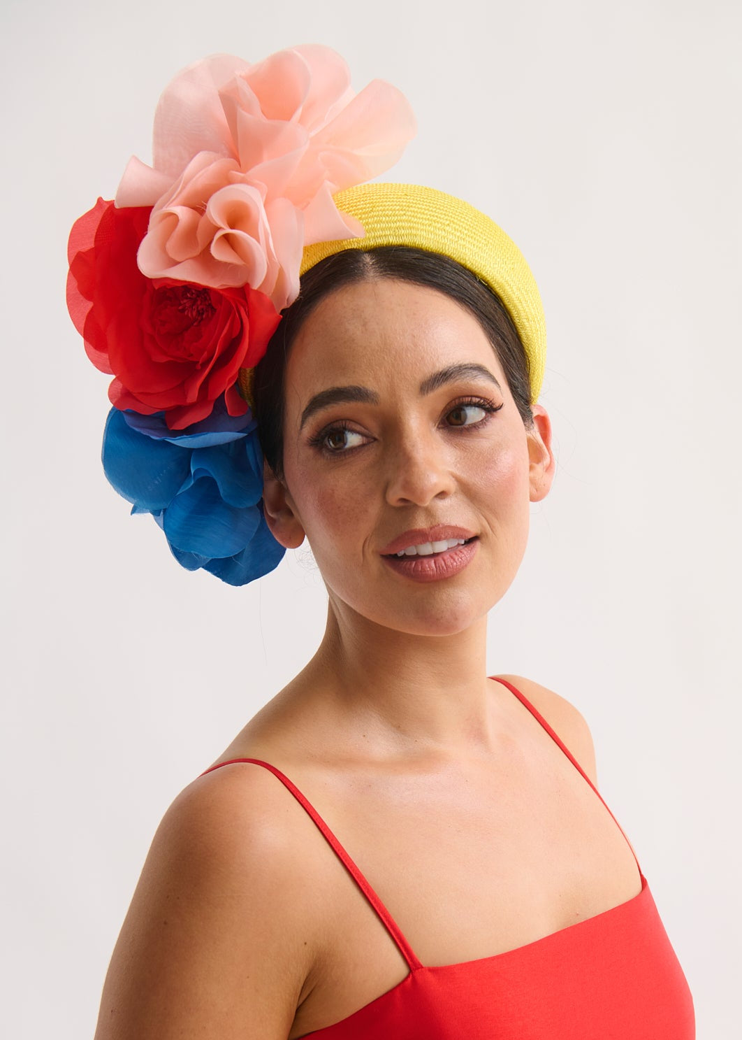 Woman wearing a colorful floral headpiece and red dress against a white background