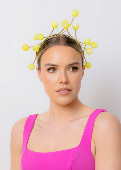 Woman wearing a bright pink dress and a decorative yellow headpiece against a plain background