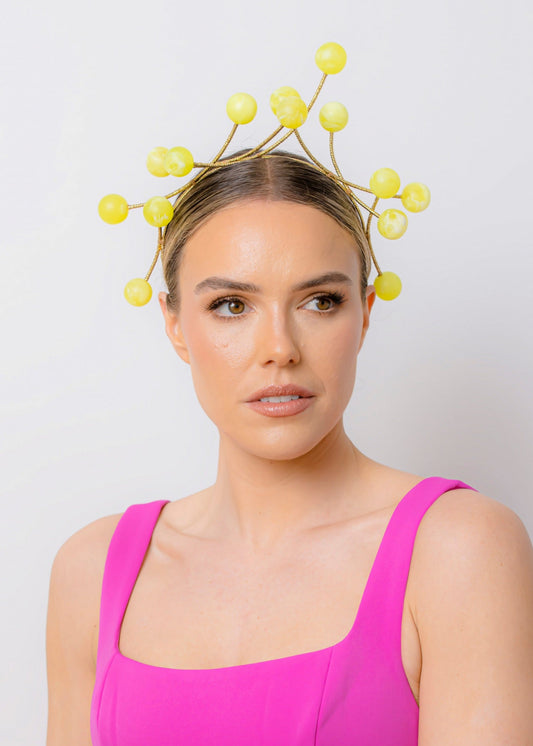 Woman wearing a bright pink dress and a decorative yellow headpiece against a plain background