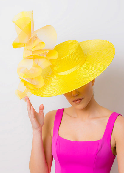 Woman wearing a bright yellow hat with ruffles and a pink dress against a white background