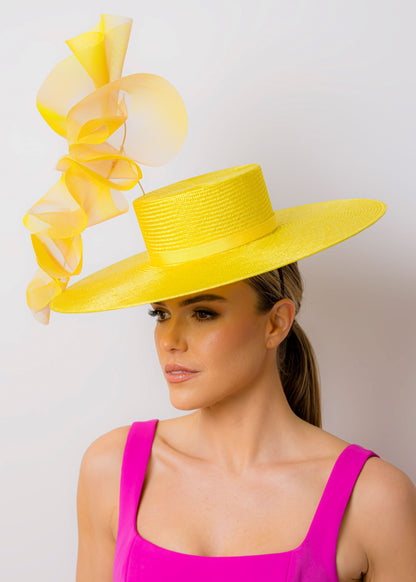 Woman wearing a bright yellow hat with large ruffles against a plain background