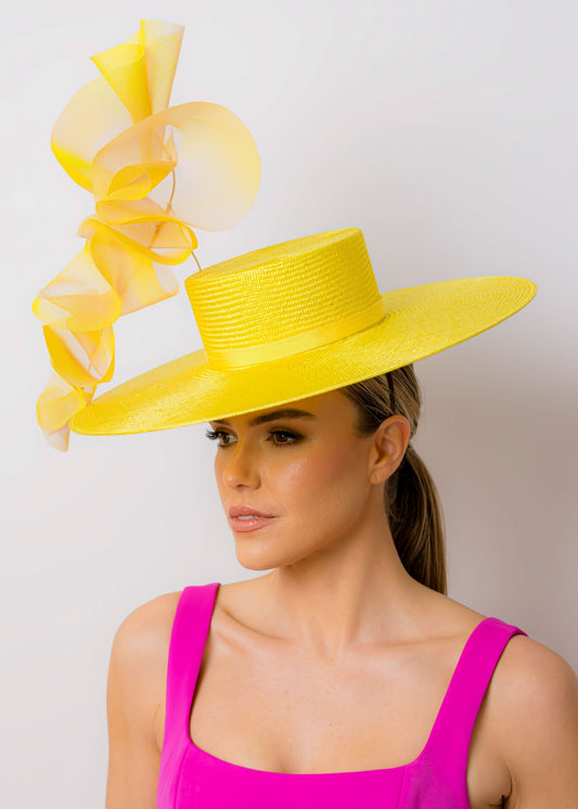 Woman wearing a bright yellow hat with large ruffles against a plain background